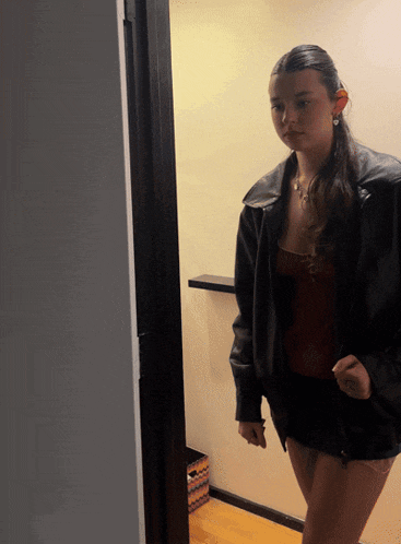 a woman in a leather jacket and shorts stands in a doorway
