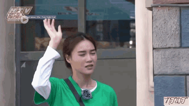 a woman in a green shirt is waving her hand in front of a building