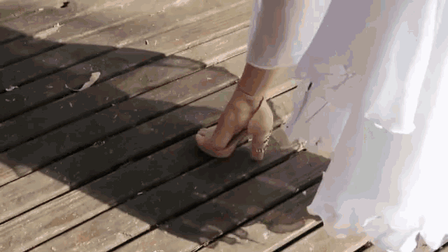 a woman in a white dress is wearing high heels on a wooden deck