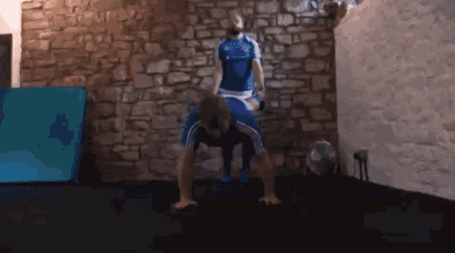 a man in a blue adidas shirt is doing push ups while another man watches