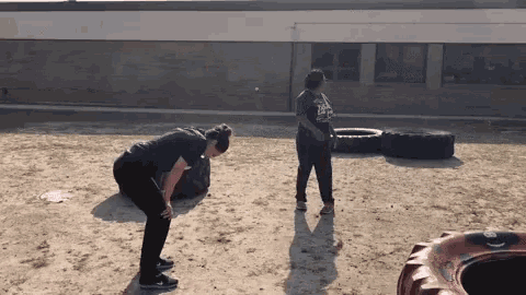 two women are doing exercises in the dirt near a tire .