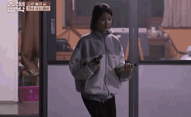 a woman in a white jacket is walking through a door holding a green bottle .