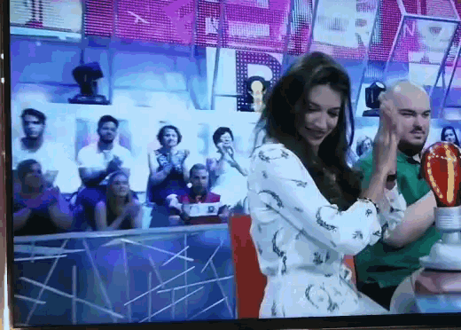 a woman in a white dress stands in front of a crowd and a trophy