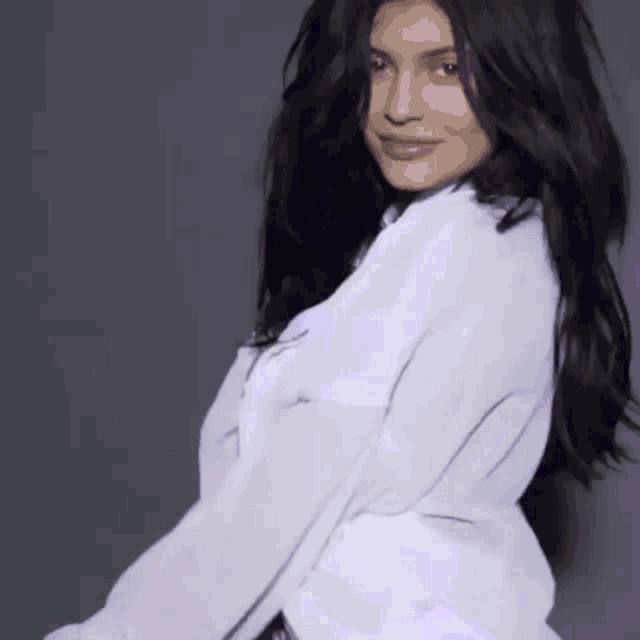 a woman with black hair is wearing a white shirt and looking at the camera .