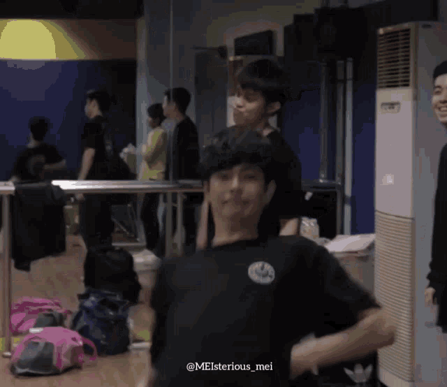 a man wearing a black shirt with a smiley face on it is standing in a room with other people