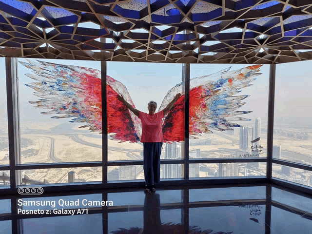 a woman stands in front of a window with wings painted on it and a samsung quad camera posneto z galaxy a71