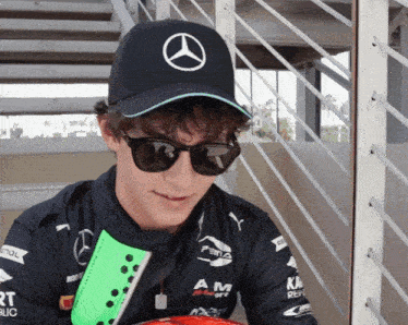 a man wearing a mercedes hat and sunglasses looks down