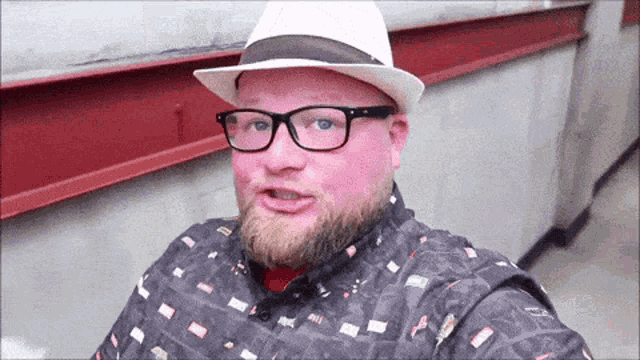 a man with a beard wearing glasses and a hat looks at the camera