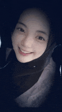 a woman wearing a black hijab and a pink jacket smiles for the camera