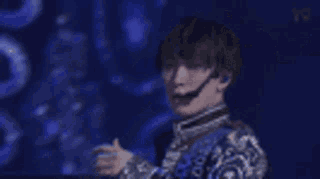 a man in a blue jacket is singing into a microphone on stage .