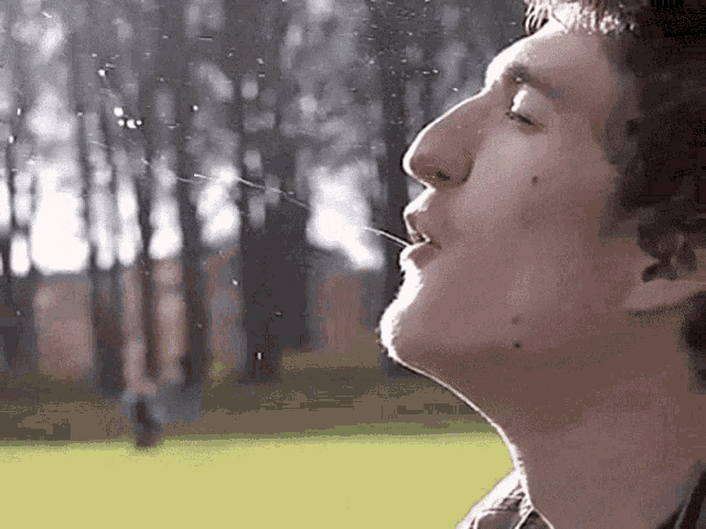 a man is drinking water from a straw in a park .