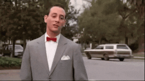 a man in a suit and bow tie is standing in front of a car on the street .