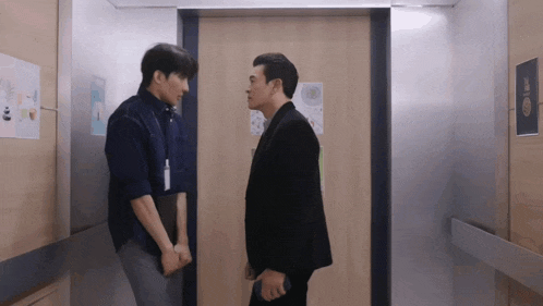 two men standing next to each other in an elevator with a sign on the wall that says ' elevator ' on it