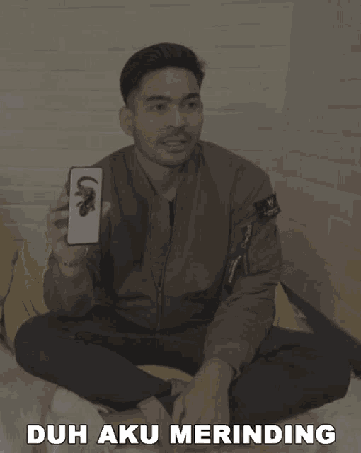 a man sitting on a bean bag chair holding a cell phone with the words duh aku merindung written below him