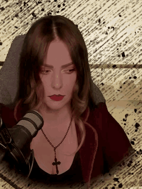 a woman wearing a black necklace with a cross on it stands in front of a microphone