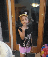 a little girl wearing a black shirt and pink shorts stands in front of a door