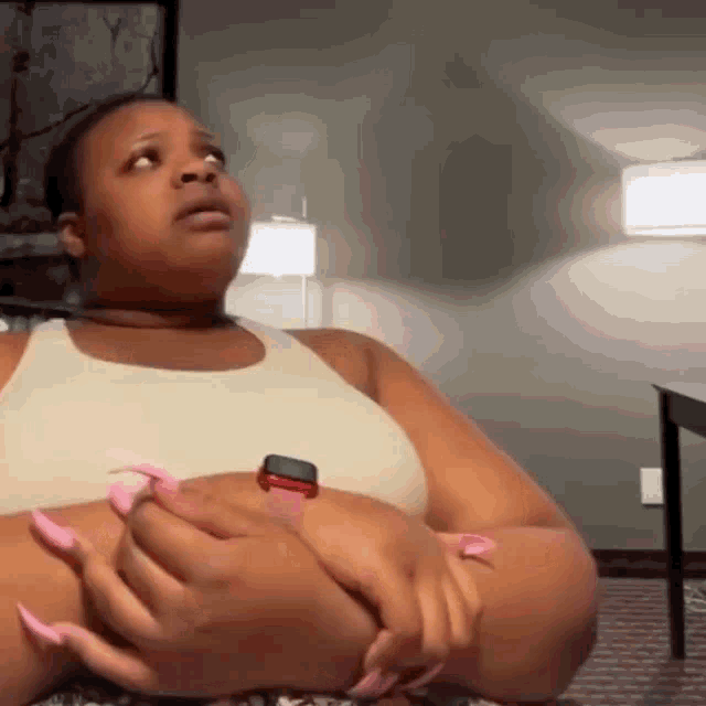 a woman with long pink nails and a watch on her wrist is sitting on the floor .