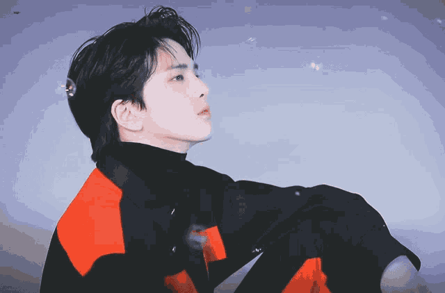 a young man wearing a red and black jacket looks up at the sky