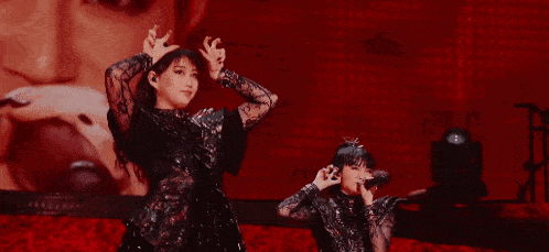 a group of women are dancing on a stage in front of a large screen with a woman 's face on it .