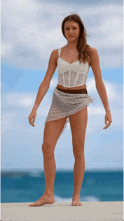 a woman in a white top and skirt is standing on a ledge near the ocean