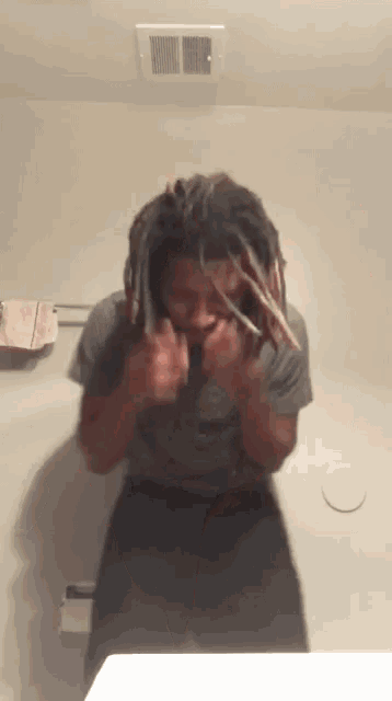 a man with dreadlocks standing in front of a bathroom mirror