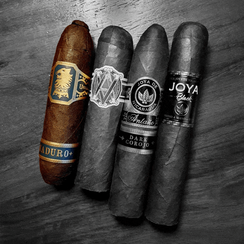four cigars are lined up on a table including joya black and antonio dark corojo