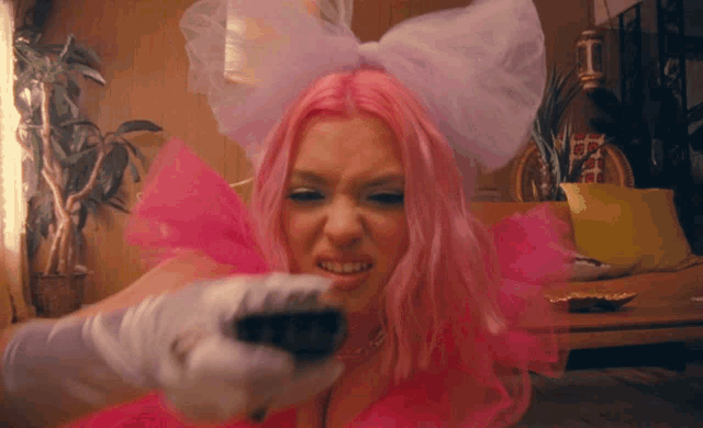 a woman with pink hair is holding a remote