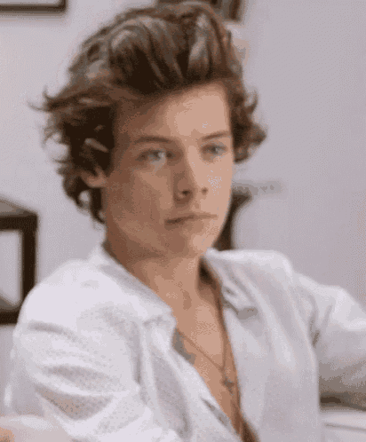 harry styles is wearing a white shirt and a necklace with a cross on it .
