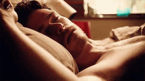 a shirtless man is sleeping in a bed with his eyes closed and his arms outstretched .