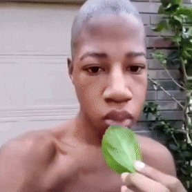 a shirtless man is eating a green leaf with his mouth