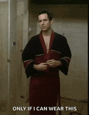 a man in a robe is standing in a bathroom and says only if i can wear this .