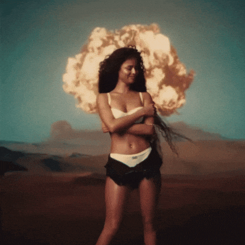 a woman in underwear stands in front of an explosion in the desert