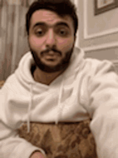 a man with a beard wearing a white hoodie is taking a selfie .