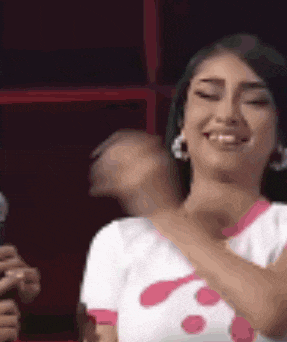 a woman is smiling and dancing in front of a microphone while wearing a pink and white shirt .