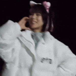 a woman in a white coat with cat ears on her head is making a heart shape with her hands .