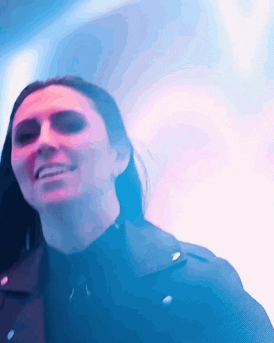 a woman in a black jacket is smiling in front of a blue light