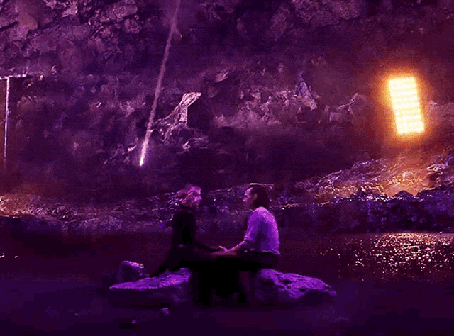 a man and a woman are sitting on a rock holding hands in front of a fire explosion .