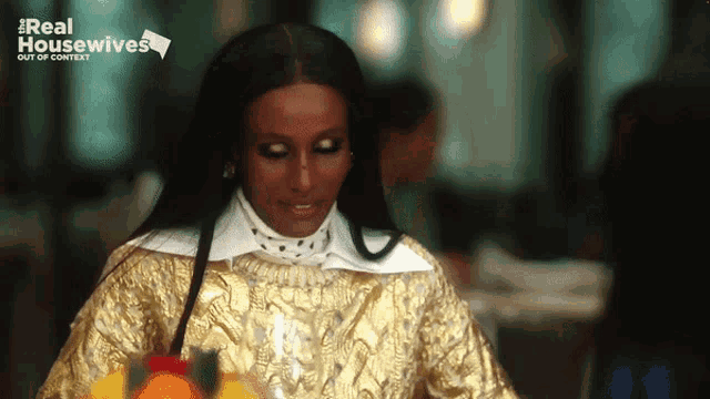 a woman in a gold dress is sitting at a table with a real housewives logo behind her