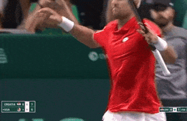 a man in a red shirt is holding a tennis racquet during a game between croatia and usa