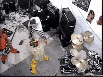 a man is playing a guitar in a room with a drum set and a clown .