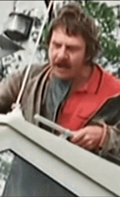 a man with a red shirt and a mustache is looking out a car window