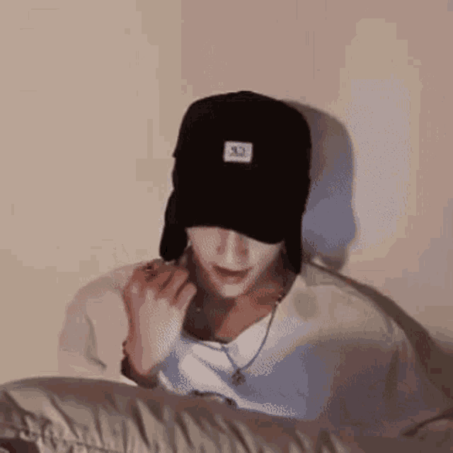 a man wearing a hat and a necklace is sitting on a bed .