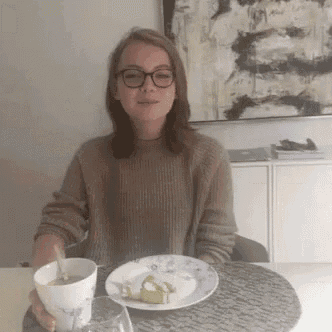 a woman wearing glasses is sitting at a table with a plate of food .
