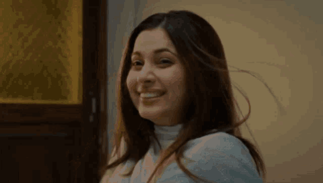 a woman with long brown hair is standing in front of a mirror and looking at the camera .