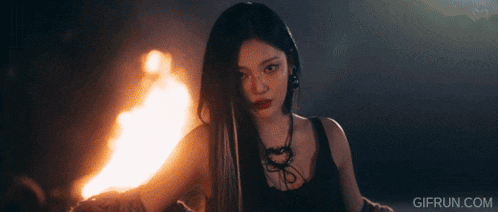 a woman is holding a torch in front of a fire and the website gifrun.com is below her
