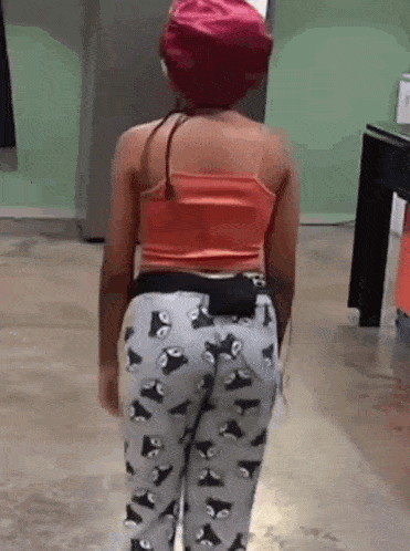 a little girl wearing a red hat and a pair of pants with owls on them is standing in a room .