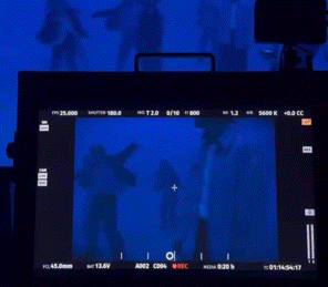 a screen shows a group of people dancing in front of a blue backdrop