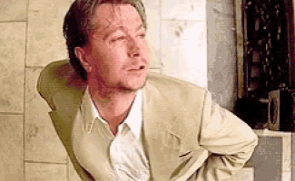 a man in a suit and white shirt is standing with his hands on his hips and looking at the camera .