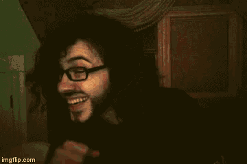 a man with glasses and a beard smiles in a dark room ..
