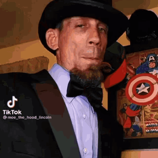 a man in a top hat and bow tie is standing in front of a picture of captain america .